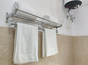 A bathroom with a towel rack holding two white towels, a shower head, and a wall-mounted faucet. - Tulin Heritage Bungalow (Purulia)
