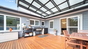 A covered patio with a grill, seating area, and large windows. - 4-Bed Family Home with Spacious Backyard and BBQ (Curtin)