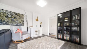A modern living room with a grey sofa, a white shag rug, a fireplace, a bookshelf, and a large abstract painting. - 4-Bed Family Home with Spacious Backyard and BBQ (Curtin)