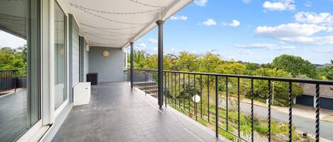 A balcony with a view of a road and greenery, a covered area with a clock, and a railing.