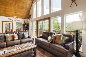 A spacious living room with a high ceiling, large windows, a leather sofa, and a wooden coffee table. - Moonlight Pines by Velo (Angel Fire)