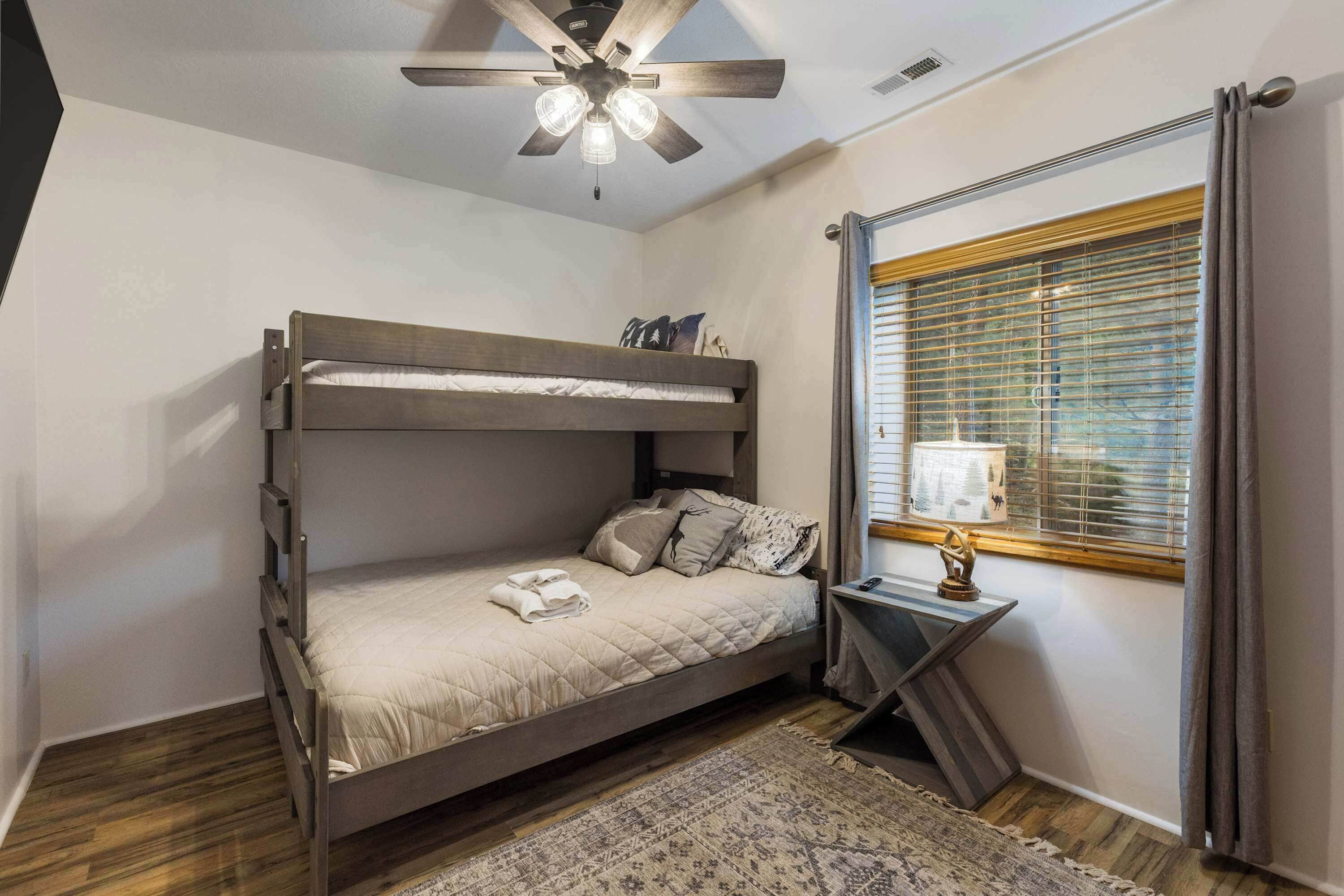 Una cama individual en literas con ventilador de techo, una ventana con persianas y una mesita de noche con lámpara.
