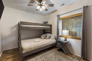 A bunk bed with a ceiling fan, a window with blinds, and a small bedside table with a lamp. - Moonlight Pines by Velo (Angel Fire)