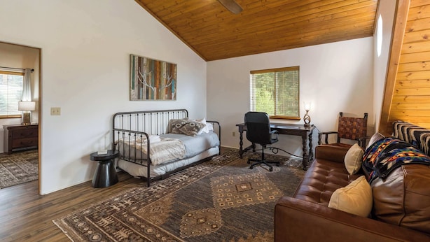 Une pièce comprenant un lit, un bureau, un canapé en cuir, un tapis et un ventilateur de plafond.