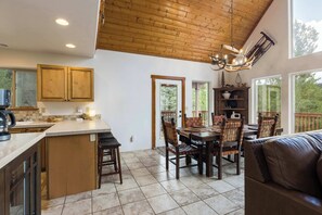 A spacious kitchen with wooden cabinets, a dining area with a large table and chairs, and a view through the windows. - Moonlight Pines by Velo (Angel Fire)