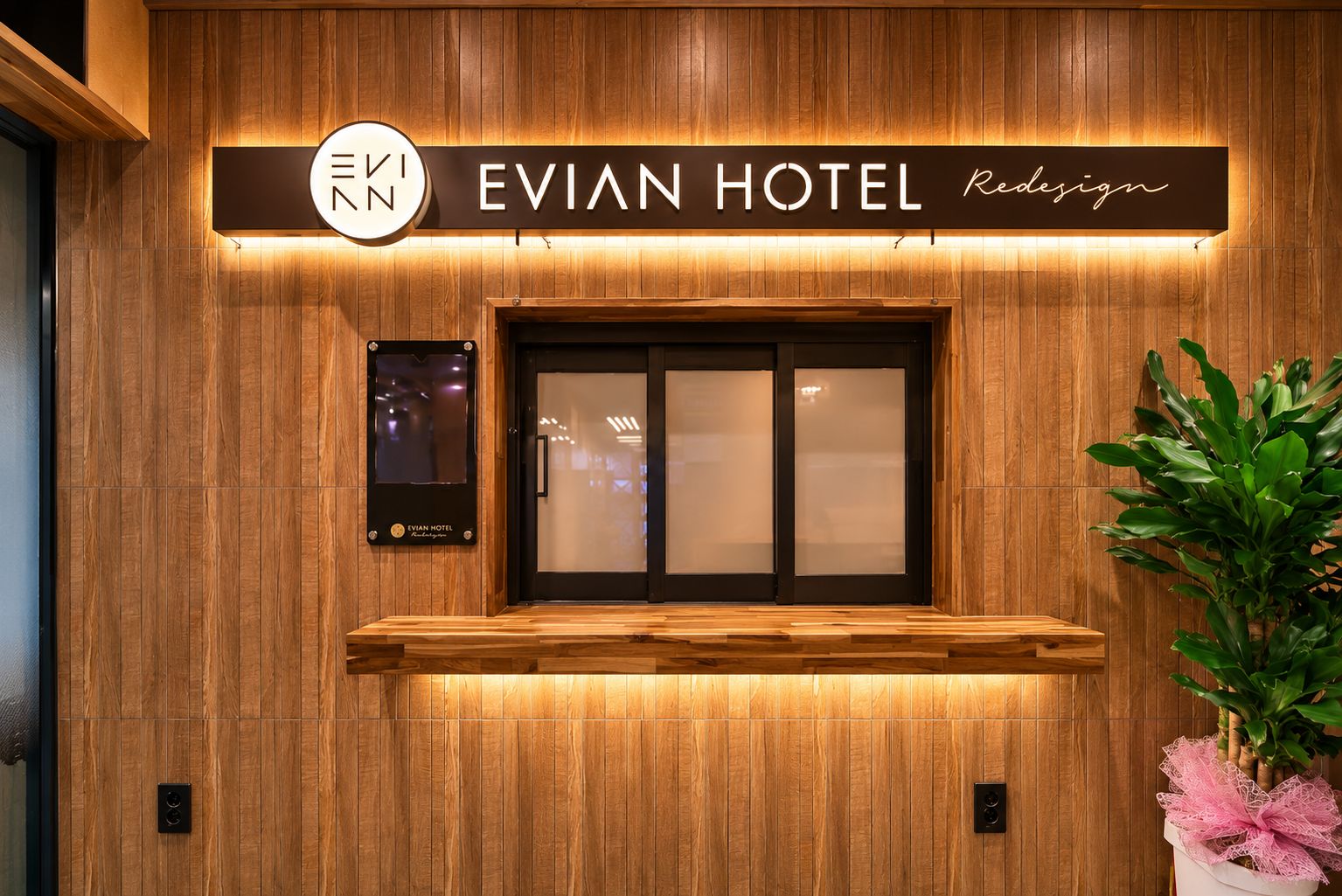 Un mostrador de recepción de madera con un letrero que dice 'EVIAN HOTEL' y una planta en maceta a la derecha.