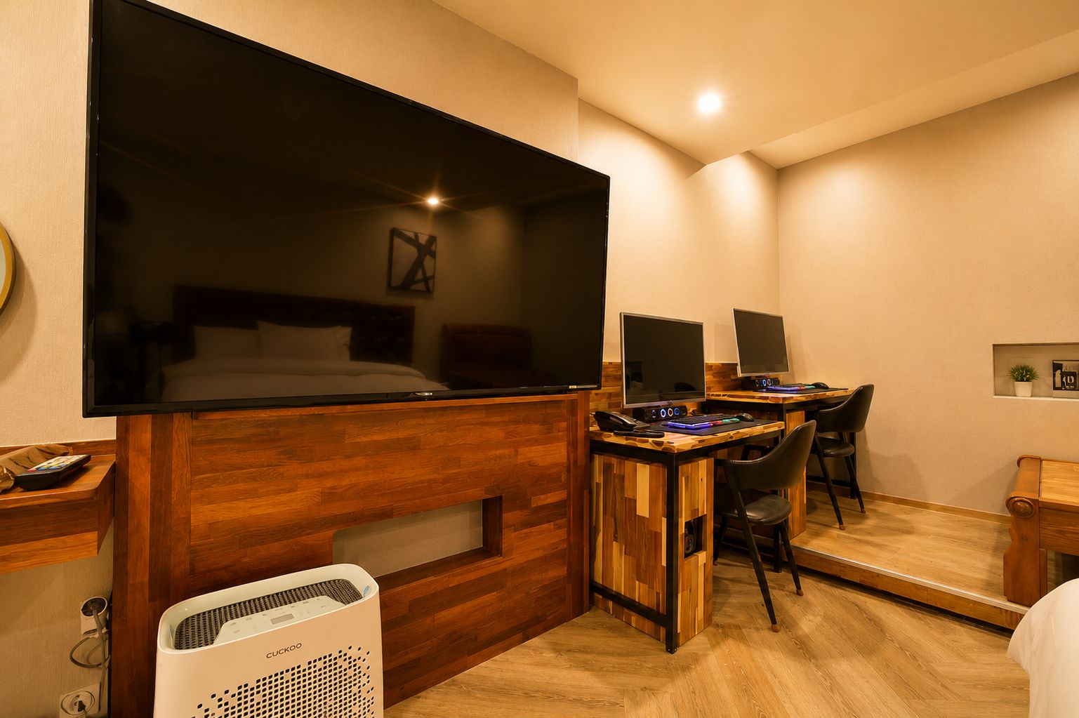 Een compacte hotelkamer met een groot bed, een bureau met twee monitoren, een stoel en een verwarming.
