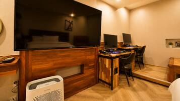 Een compacte hotelkamer met een groot bed, een bureau met twee monitoren, een stoel en een verwarming.
