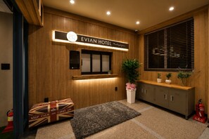 A hotel reception area with a wooden panel wall, a reception desk, a potted plant, a fire extinguisher, and a fire hose. - Evian Hotel (Gyeongsan)