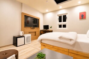 A modern hotel room with a large bed, a flat-screen TV, a desk with a computer, and a small kitchenette area.
