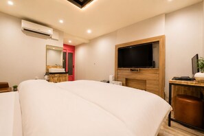 Une chambre d’hôtel avec un lit, un téléviseur fixé au mur, un bureau avec un ordinateur et une petite plante.