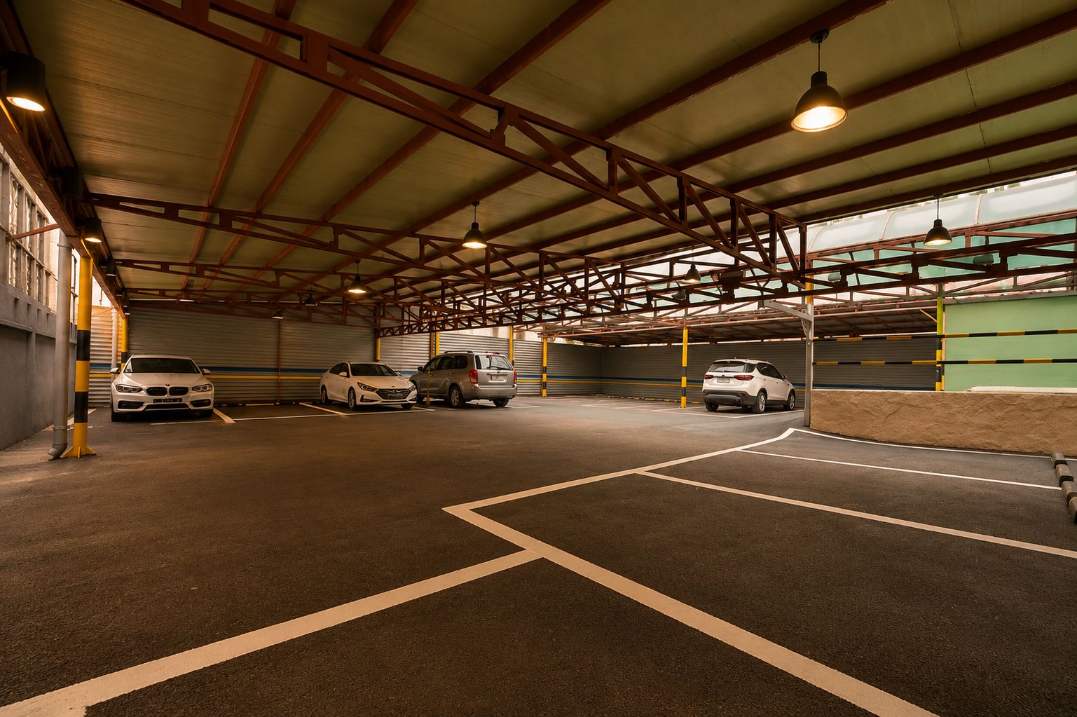 Un estacionamiento cubierto con tres coches aparcados, vigas metálicas e iluminación en el techo.