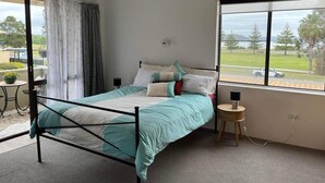 Quarto com cama, ventilador de teto, janela com vista para o exterior e uma mesinha de cabeceira com abajur.