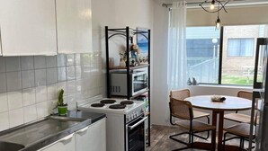 Uma cozinha compacta com armários brancos, um fogão e micro-ondas. Há uma área de jantar com uma mesa redonda e cadeiras.