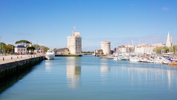 Un port doté d’une tour imposante et d’une structure ressemblant à un château, entouré d’eaux calmes et de bateaux.