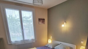Une chambre à coucher avec un lit, des lampes de chevet, une fenêtre, un radiateur, un bureau et une chaise.