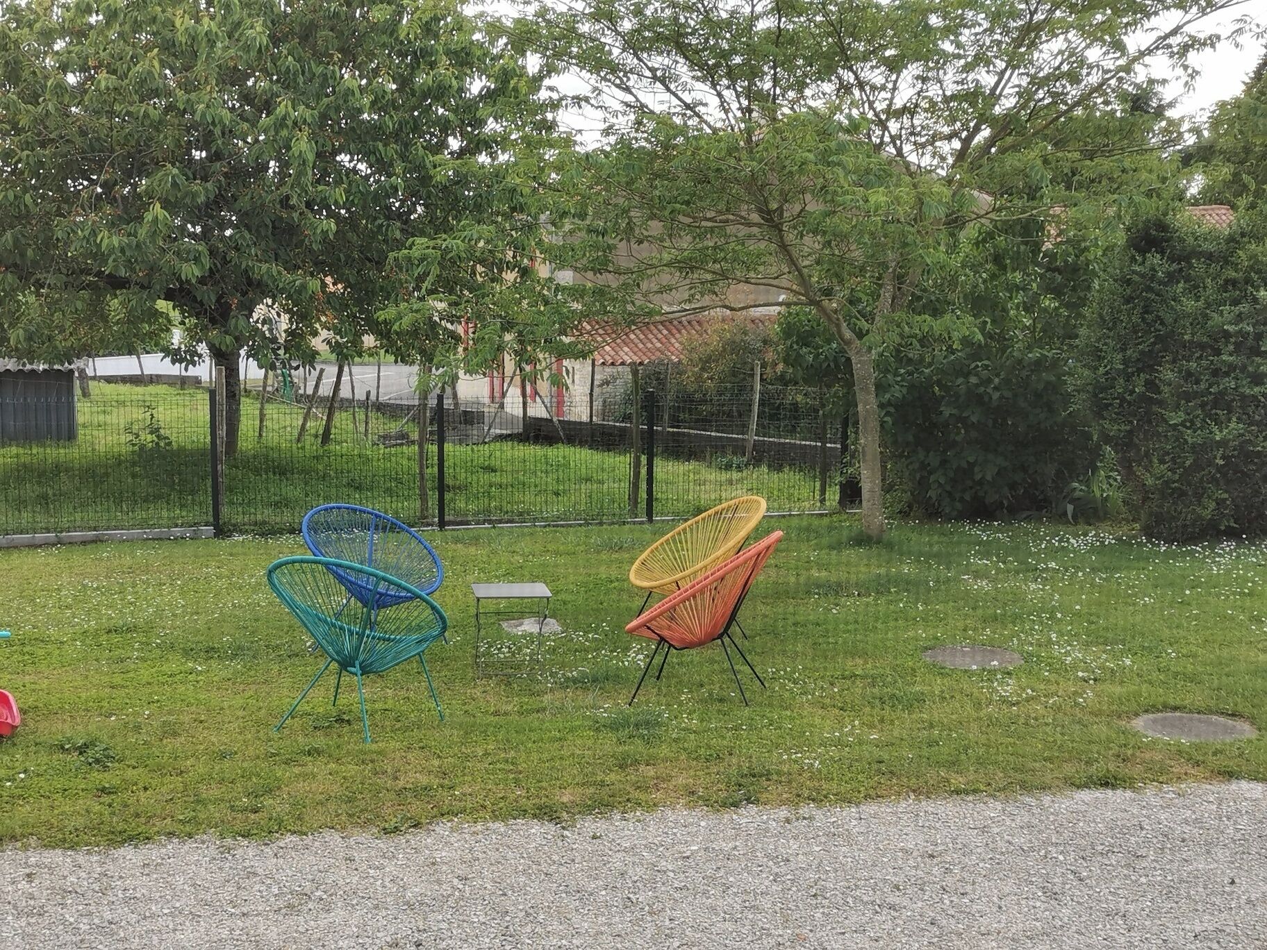 Un espace extérieur verdoyant avec deux chaises colorées et une clôture en arrière-plan.
