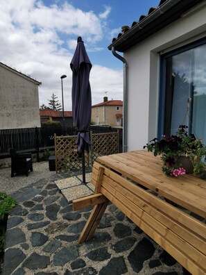 Eine Terrasse mit Holztisch und Bänken, einem violetten Sonnenschirm und einem Blumentopf.