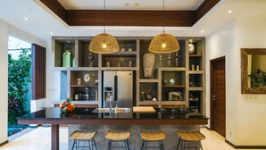 Une cuisine moderne dotée d’un îlot central, de tabourets de bar, de luminaires suspendus et d’étagères intégrées où sont exposés des objets décoratifs.