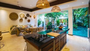 Une cuisine moderne dotée d’un îlot central, d’un coin repas avec un canapé et des fauteuils, et d’une grande fenêtre donnant sur un jardin luxuriant.