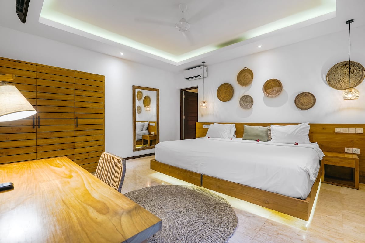 Un dormitorio moderno con una cama grande, cabecera de madera, mesitas de noche, alfombra redonda y adornos en la pared.