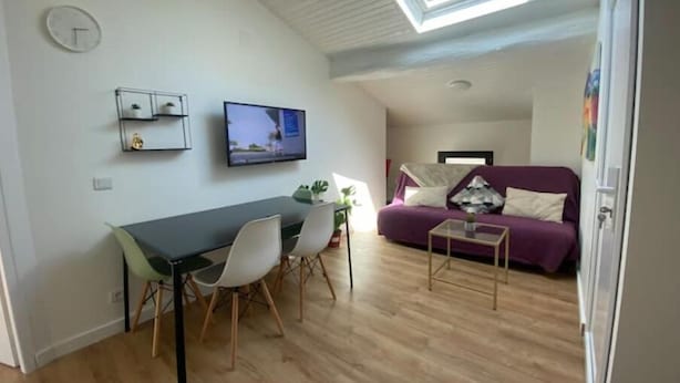 Un salon moderne comprenant un coin repas, un canapé violet, un téléviseur et une lucarne.