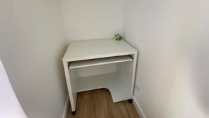 Un petit bureau blanc, placé dans un coin d’une pièce dont le sol est recouvert de parquet.