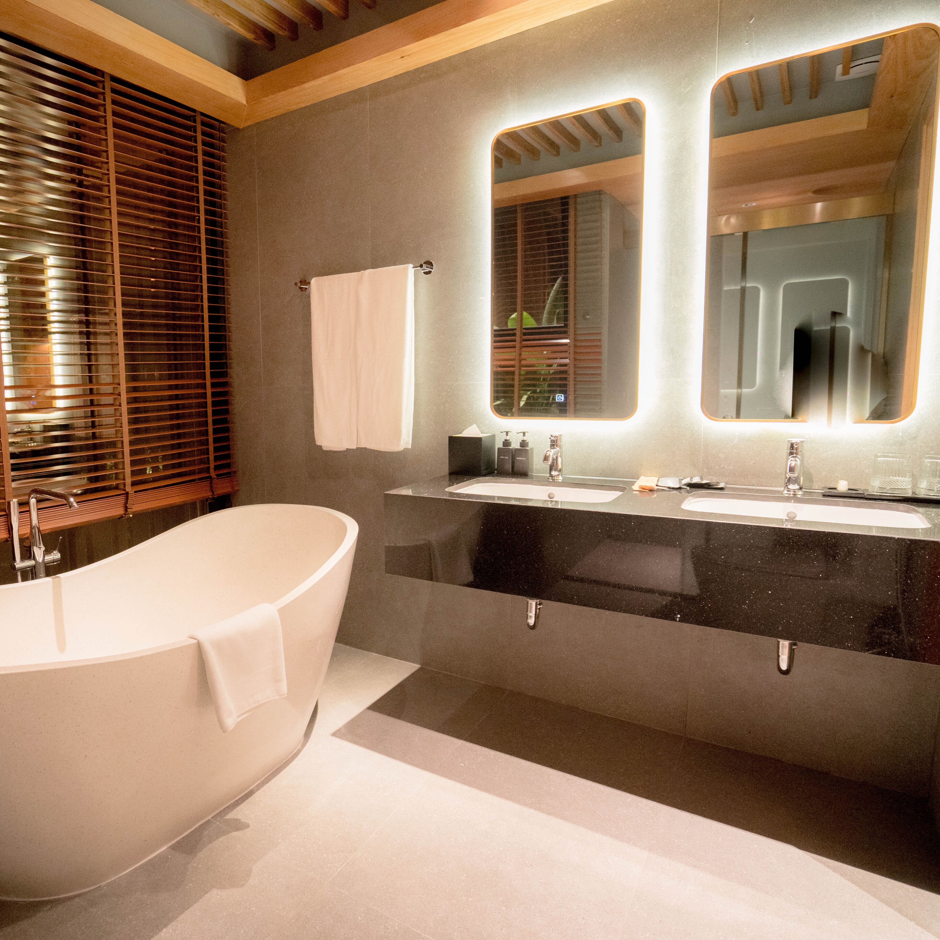 A modern bathroom with a freestanding bathtub, a vanity with a mirror, and a window with blinds.