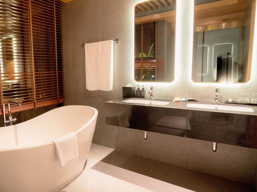 A modern bathroom with a freestanding bathtub, a vanity with a mirror, and a window with blinds.