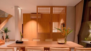 A dining area with a wooden table and chairs, a decorative screen, and a staircase in the background. - Icity Oneriver Luxury Villa (Da Nang)