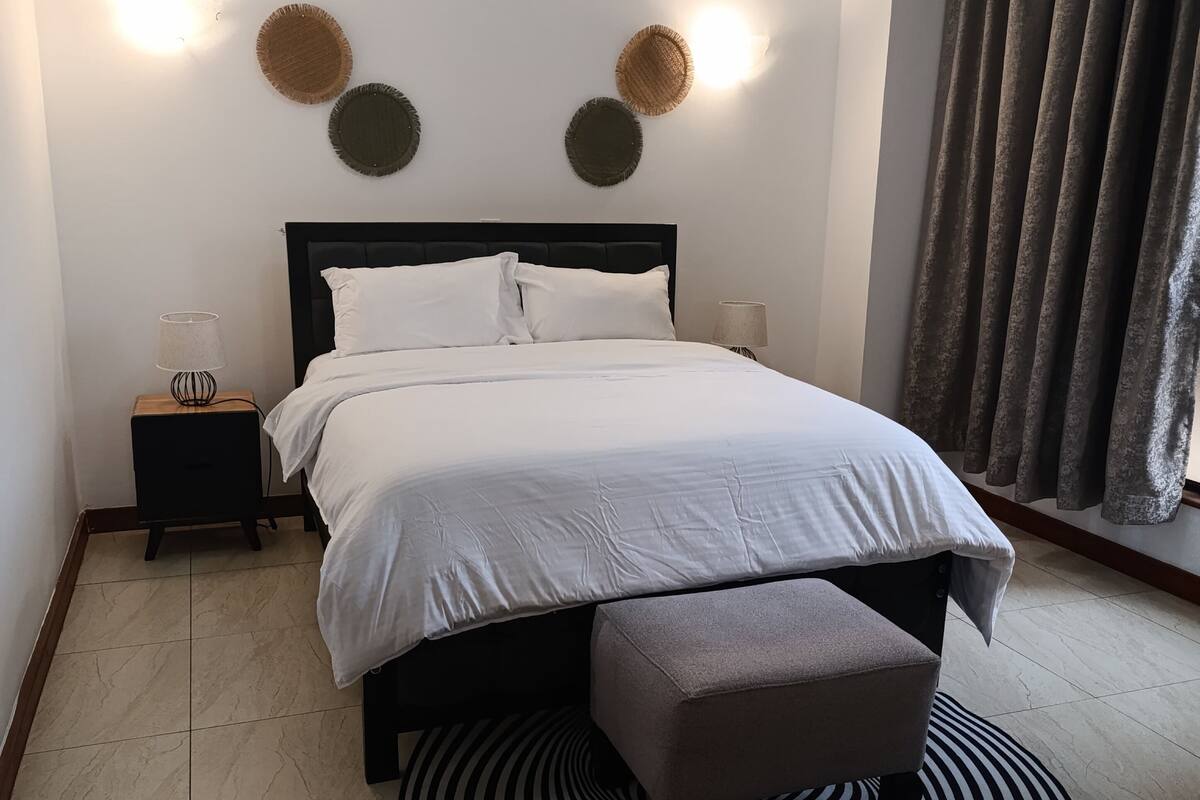 Une chambre à coucher bien rangée, avec un lit, des tables de chevet, un tapis rond et un rideau.