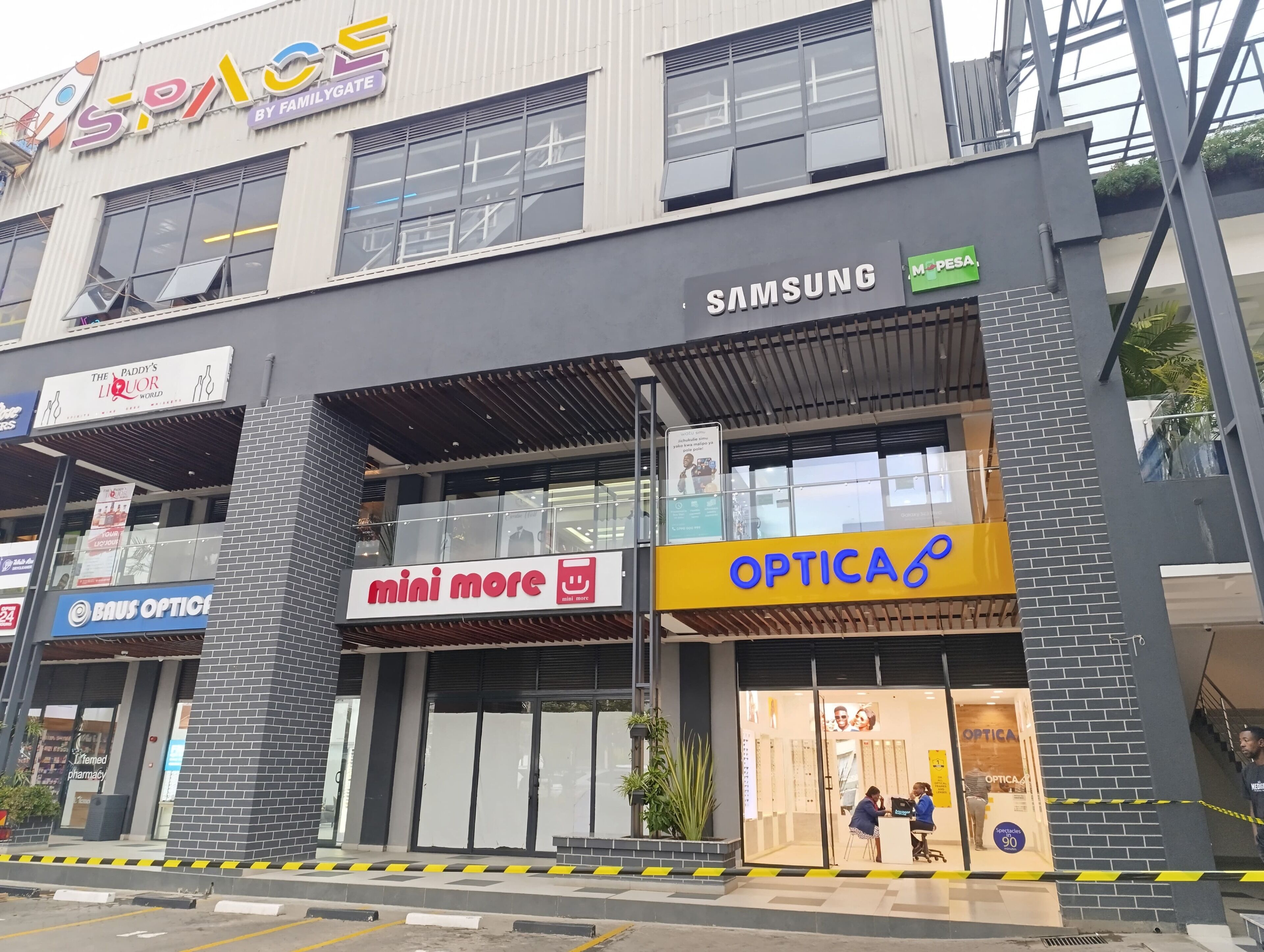 Un immeuble abritant plusieurs commerces, notamment une optique, un magasin Samsung et une pharmacie.