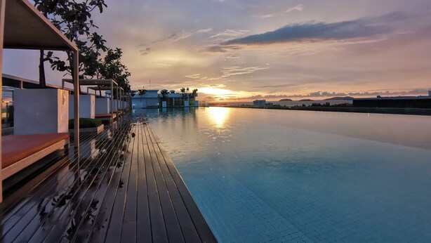 Un área de piscina tranquila con terraza de madera, con vistas a la puesta de sol sobre el agua.