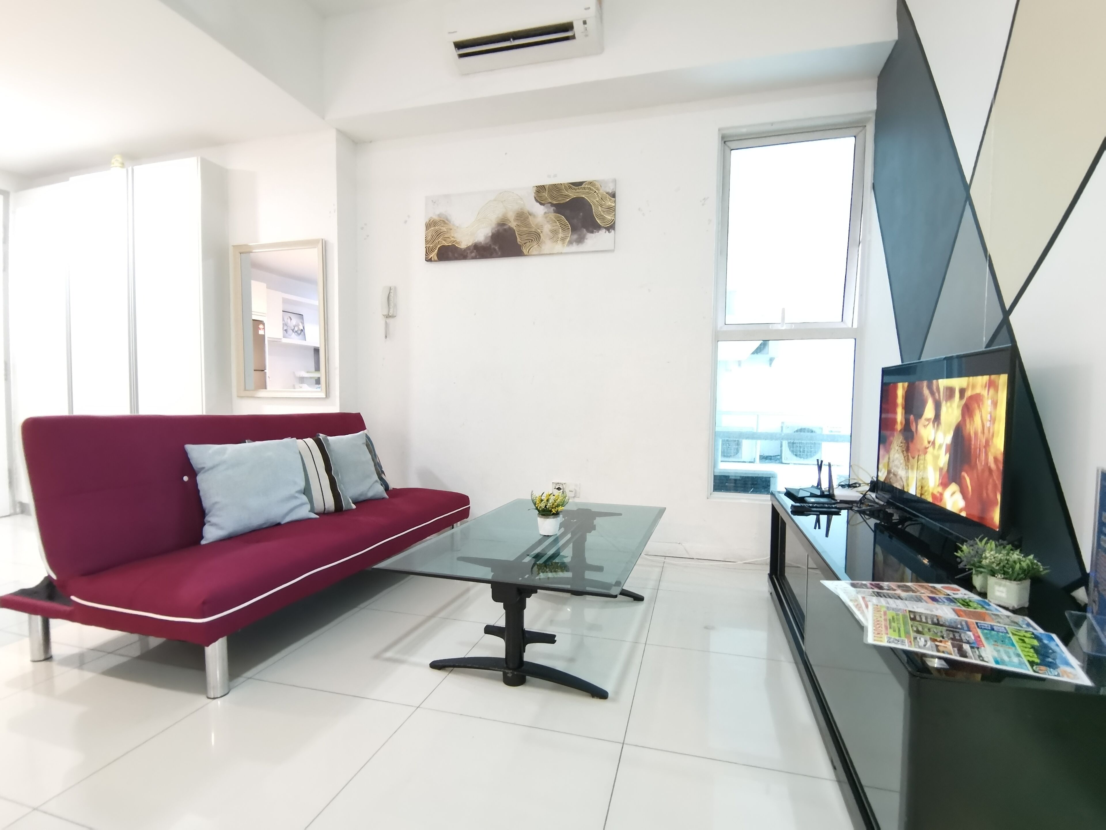 A modern living room with a red sofa, a glass coffee table, a flat-screen TV, and a magazine rack.