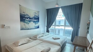 Una habitación con dos camas, piso de madera, vista al exterior, una mesa y una silla.