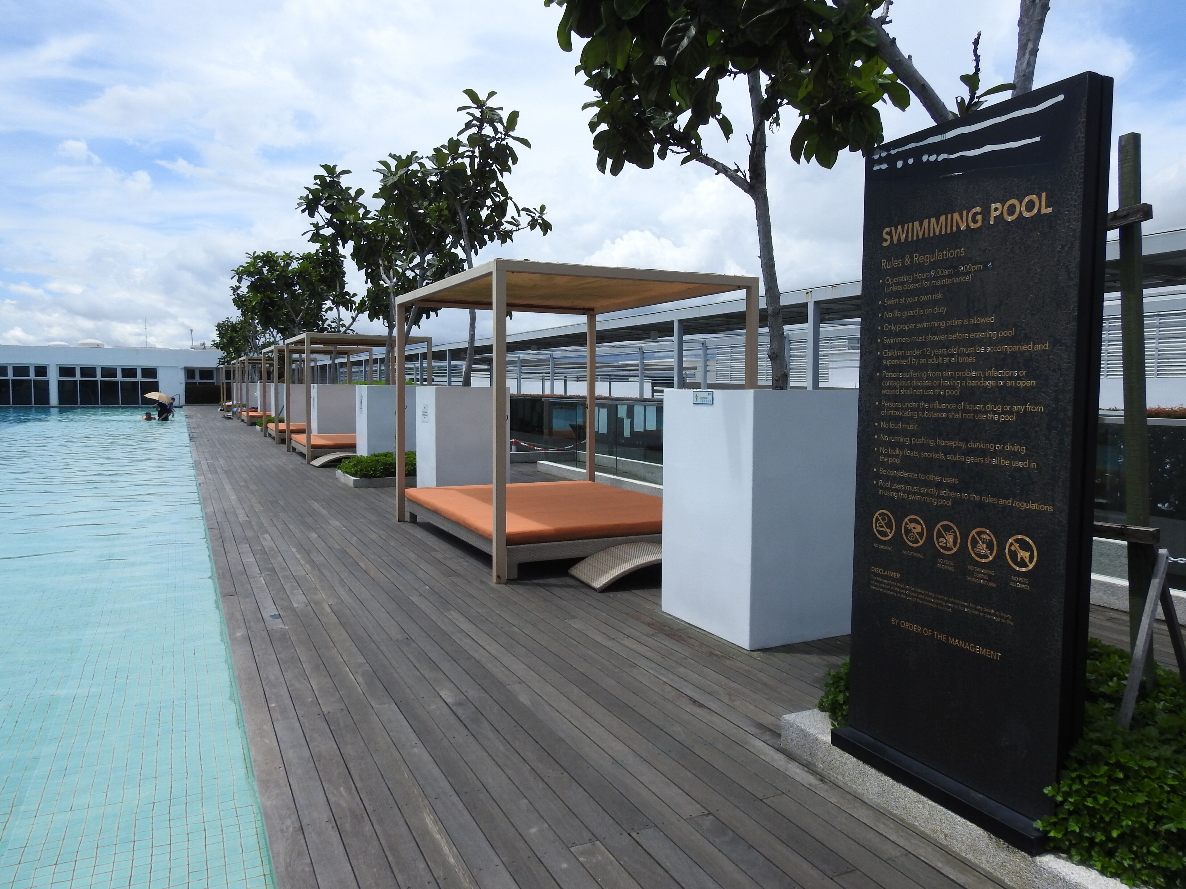 A swimming pool area with lounge chairs and a sign detailing pool rules and regulations.
