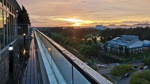 Vista al atardecer desde el balcón de un edificio, con un paseo pavimentado y una masa de agua distante.