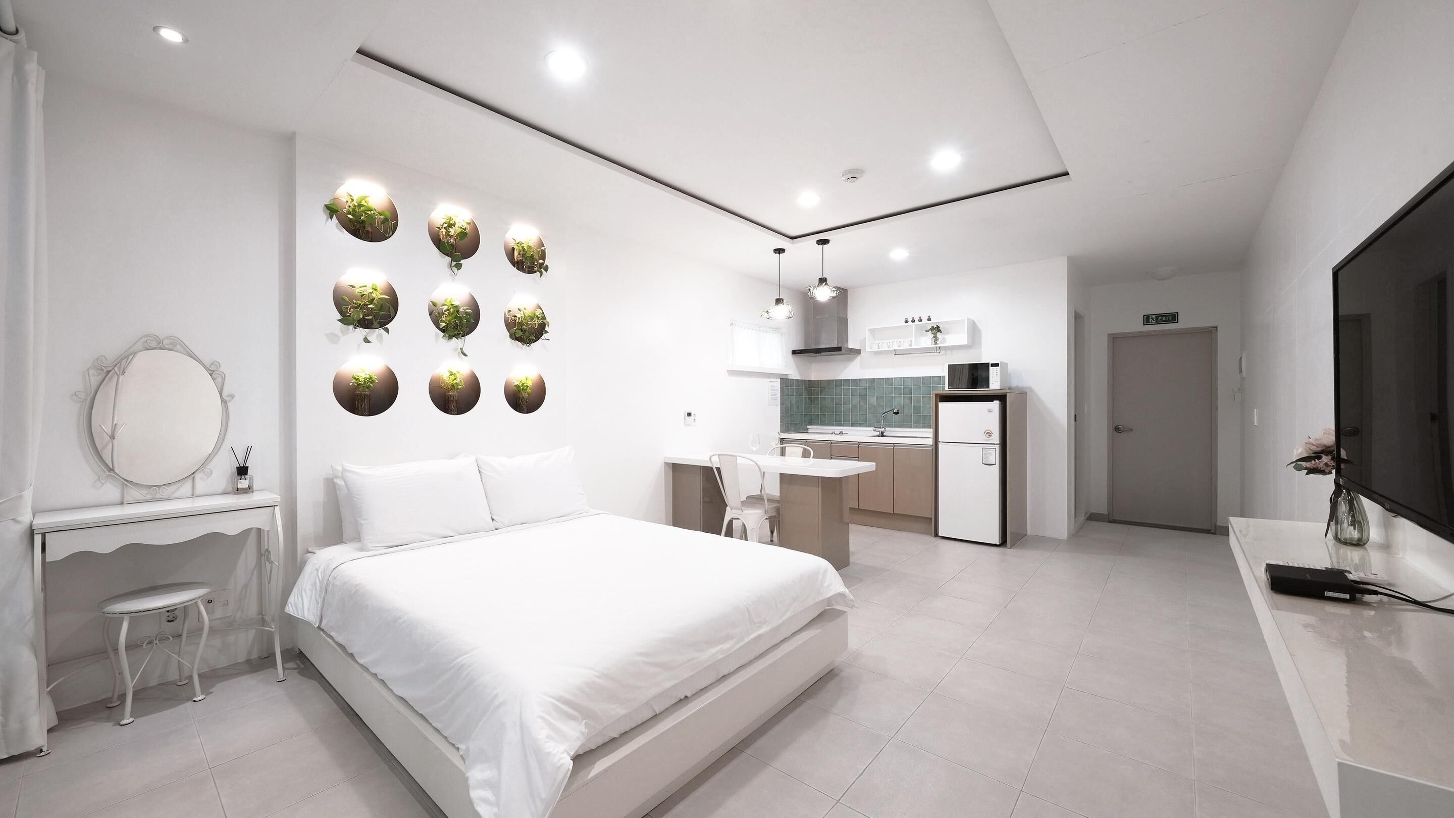 Una habitació d'hotel moderna amb un llit, una tocador amb mirall, una taula petita, un escriptori, una cuineta i un bany.