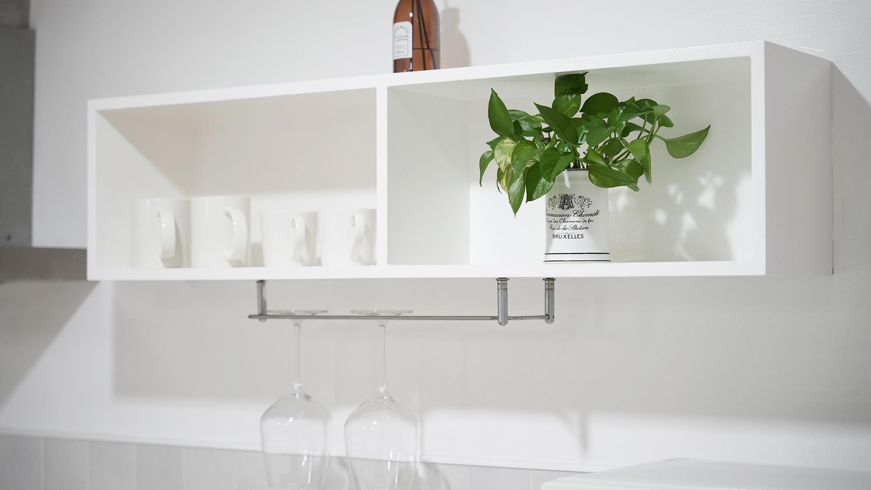 A white shelf with a potted plant and a wine bottle.