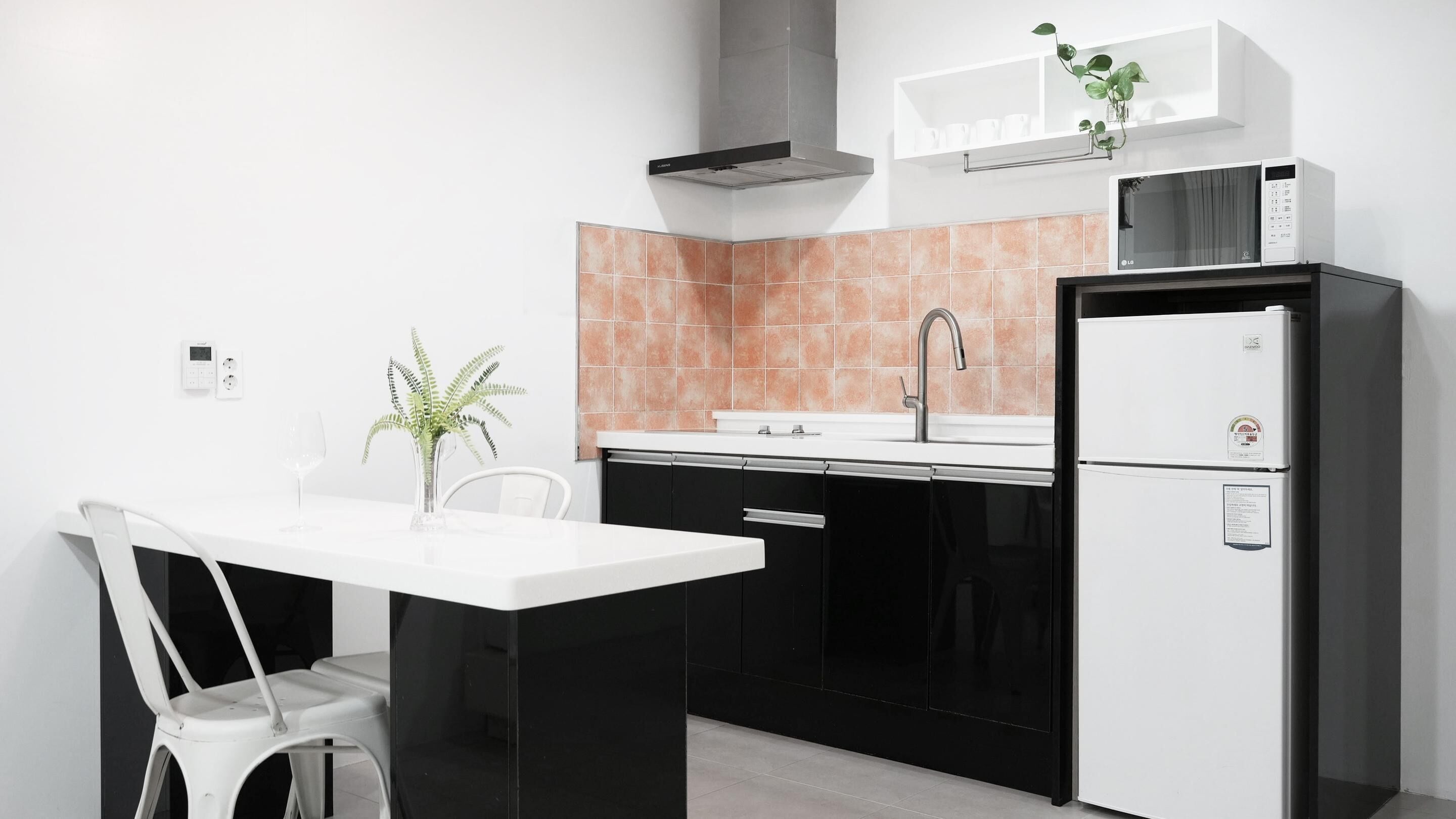 A modern kitchen with a white countertop, black cabinets, a stainless steel sink, a built-in microwave, and a refrigerator.
