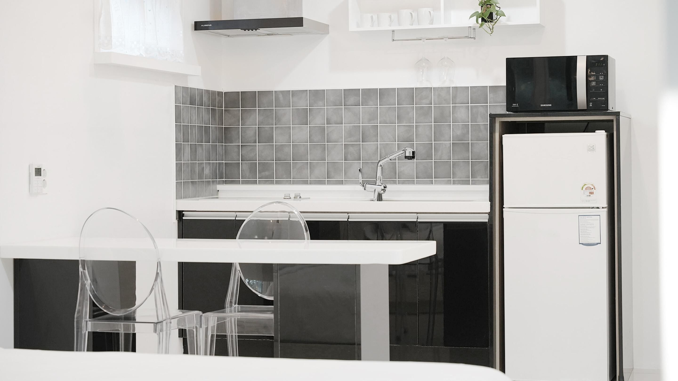 A modern kitchen with a white countertop, grey tiled backsplash, stainless steel appliances, and a clear glass table with chairs.