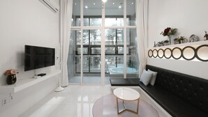 Ein modernes Wohnzimmer mit Flachbildfernseher, einer Couch, einem Couchtisch und einer Glastür zum Balkon.