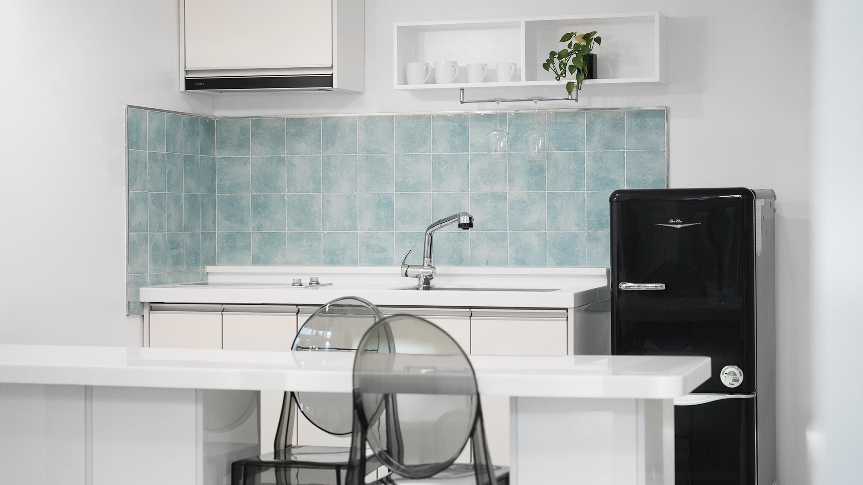 A modern kitchen with a white countertop, a sink with a chrome faucet, and a black refrigerator.