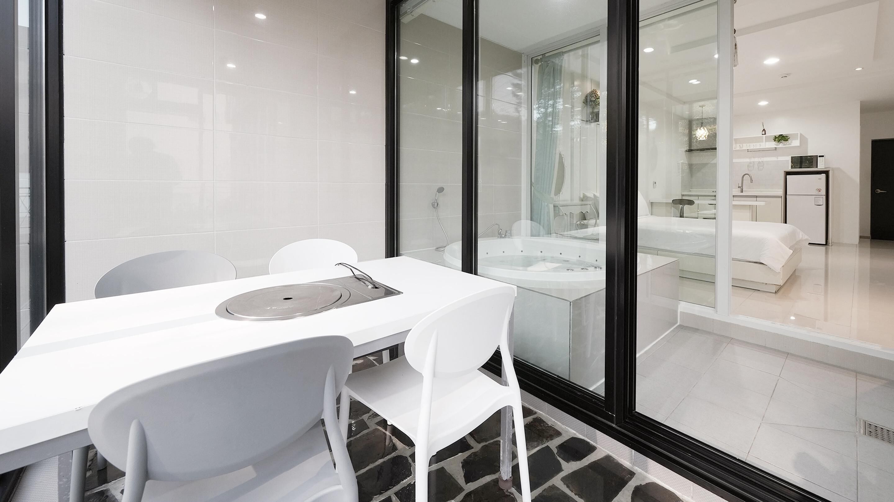 A modern hotel room with a glass partition, a white dining table, and a white sofa.
