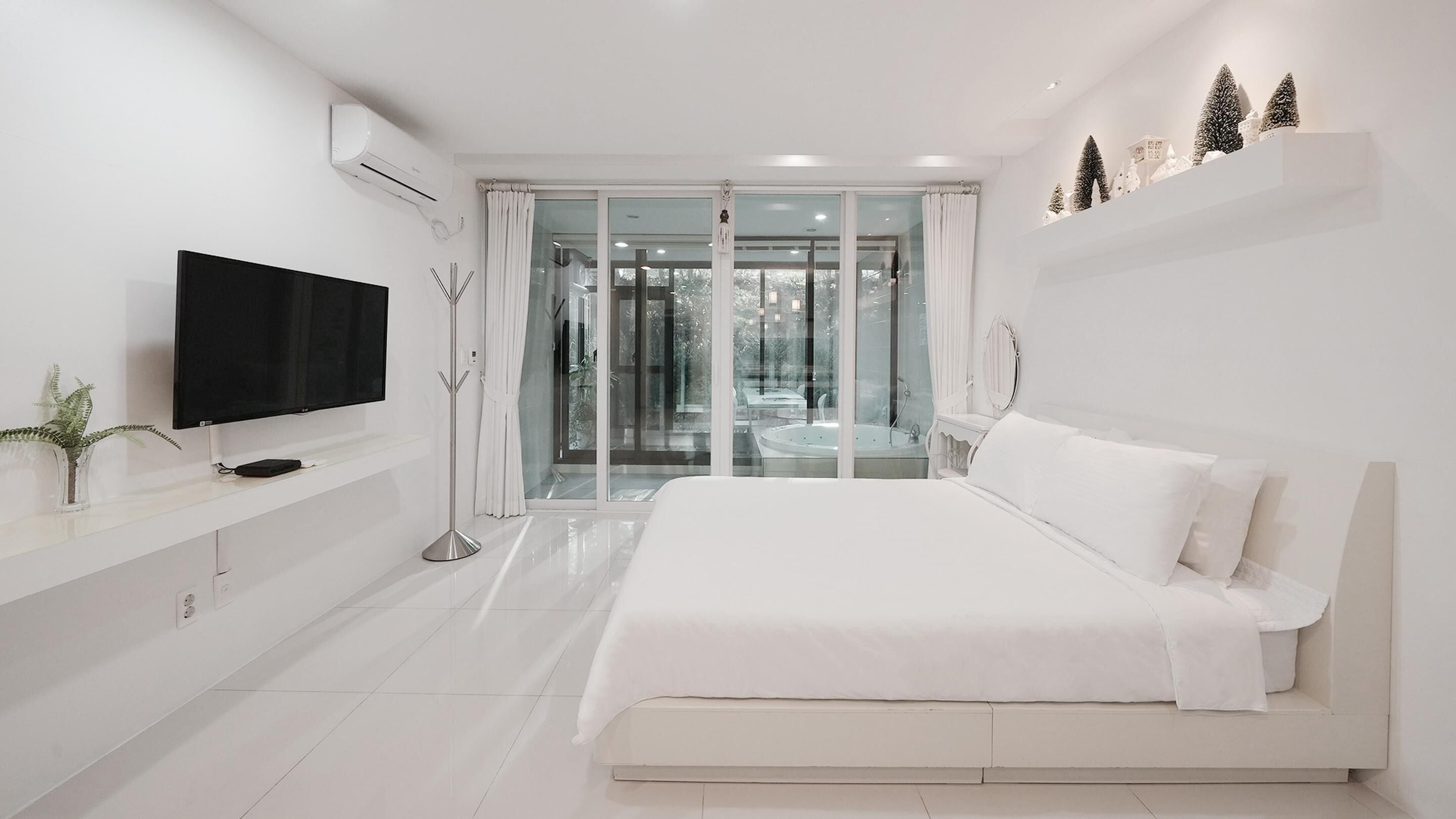 Ein modernes Schlafzimmer mit einem großen Bett, einem flachbildfernseher an der Wand und einer Glastür, die auf einen Balkon führt.