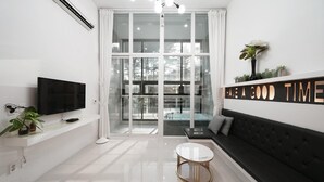 Ein modernes Wohnzimmer mit großem Fernseher, einer Couch, einem Couchtisch und einer Glastür zum Balkon.