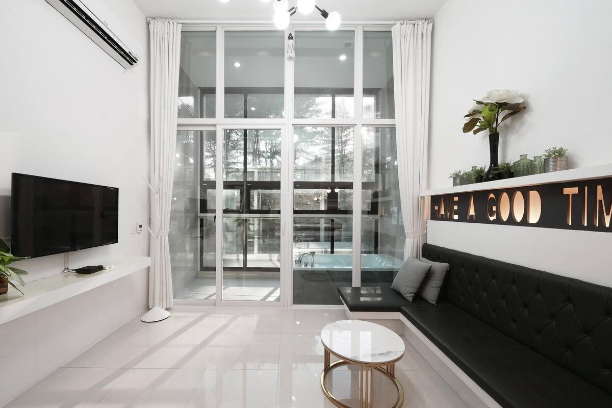 Un salon moderne avec une grande télévision, un canapé, une table basse et une porte vitrée donnant sur un balcon.