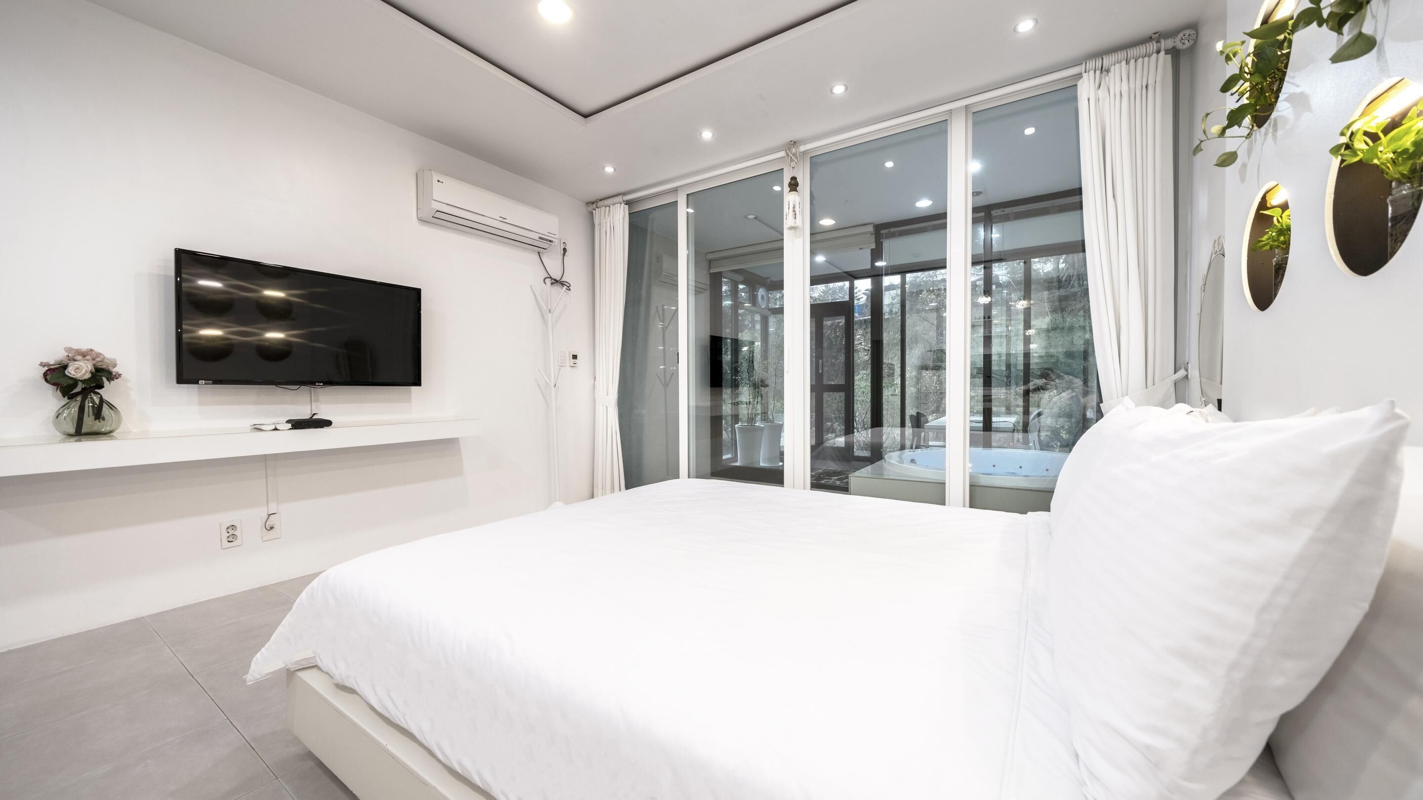 Un dormitorio moderno con una cama grande, un televisor de pantalla plana, un equipo de aire acondicionado y un ventanal corredero que da a un balcón.