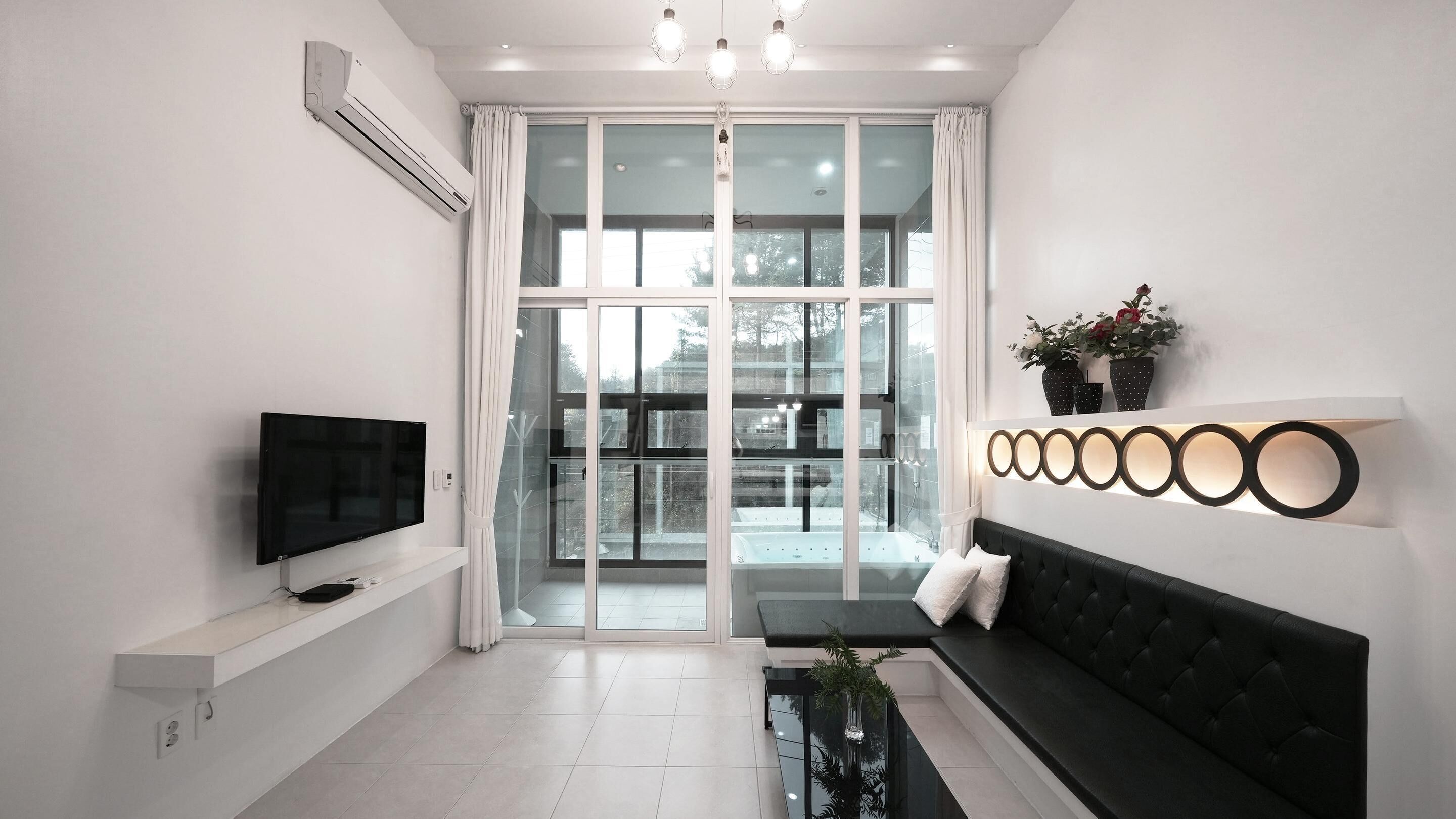 Een moderne woonkamer met een flatscreen televisie, een zwarte bank, een glazen deur naar buiten en een wandlamp.