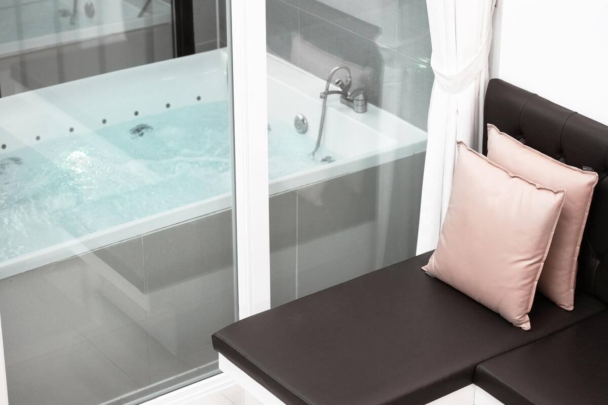 Une salle de bain moderne avec une baignoire entourée de parois en verre, un banc noir agrémenté d'un coussin rose et un espace douche bien délimité.